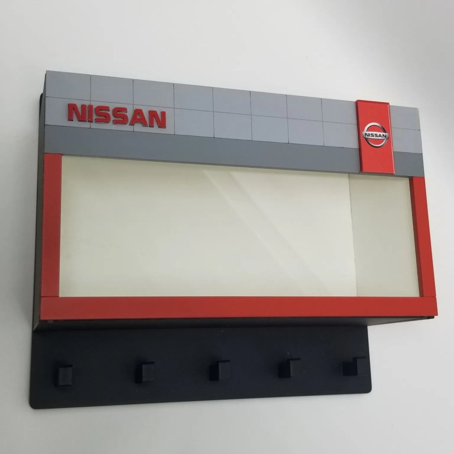 Gray and red Nissan-branded wall key hook rack with five black hooks and clear display case.
