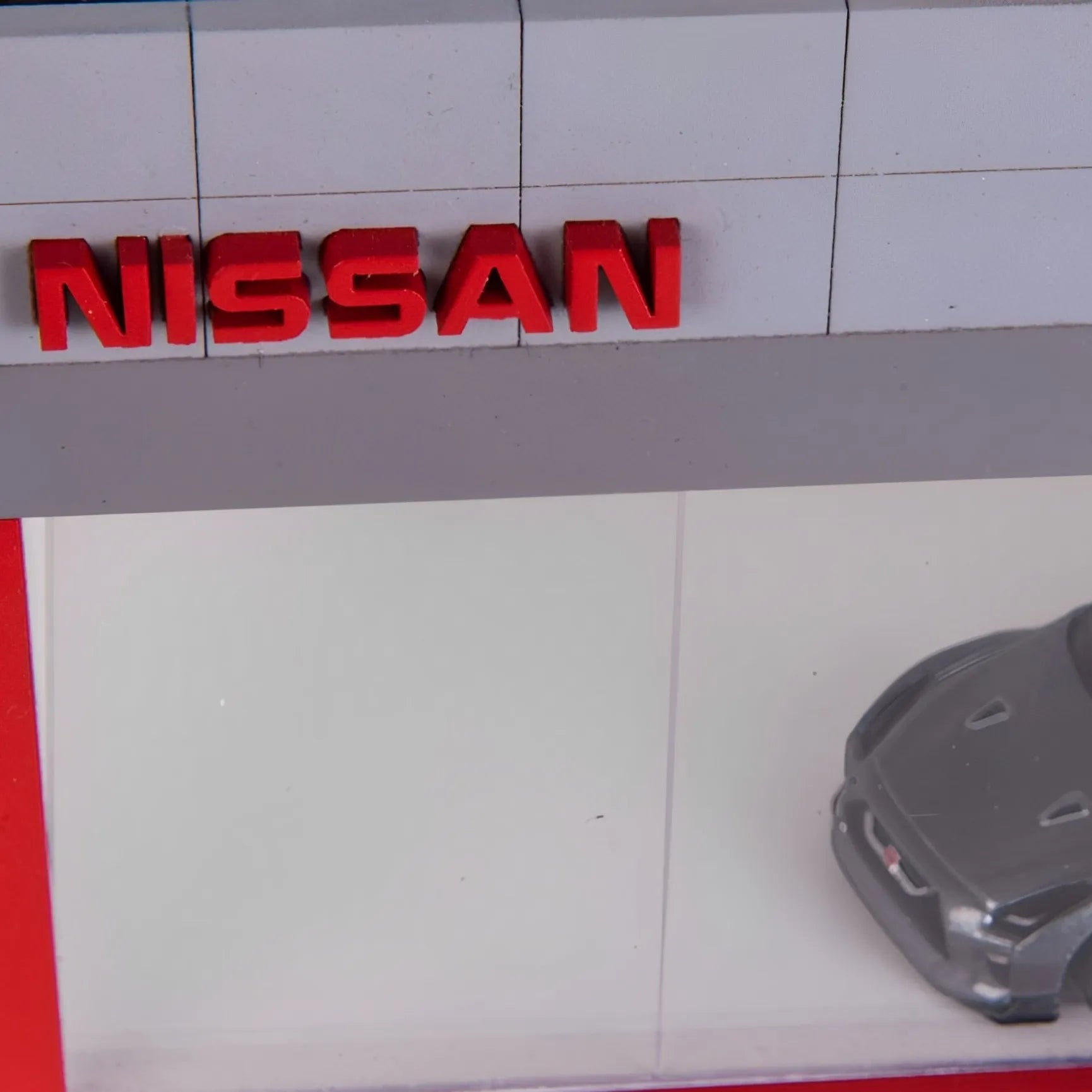 Red Nissan logo wall key hook rack with a clear display case holding a gray scale model car.