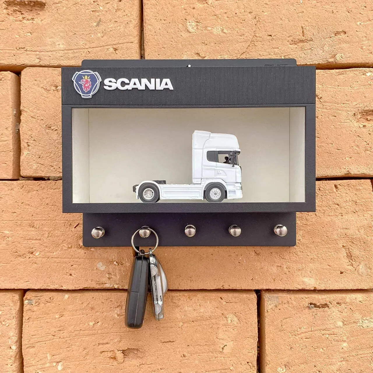 Black Scania wall key hook rack with white scale model truck and five metal hooks mounted on brick wall.
