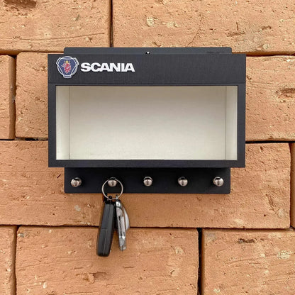 Black rectangular Scania wall key hook rack with four metal hooks and a clear display case on a brick wall.
