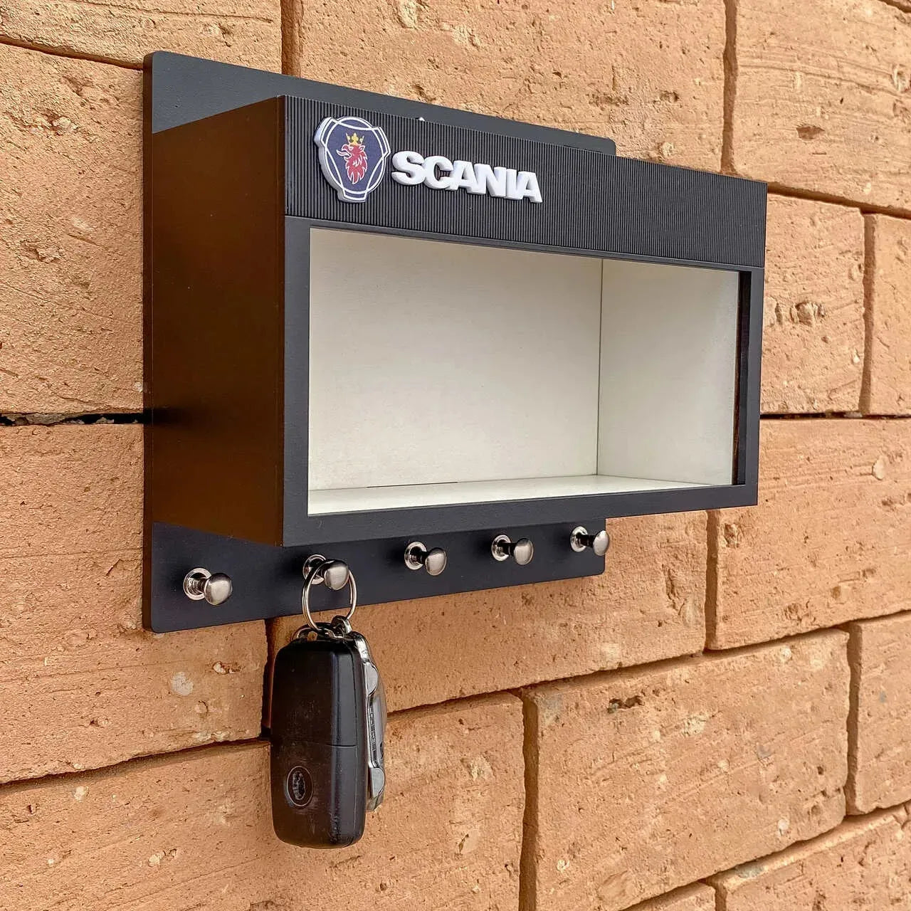 Black rectangular wall-mounted key hook rack with Scania logo and five metal hooks, holding a key fob, designed to display.