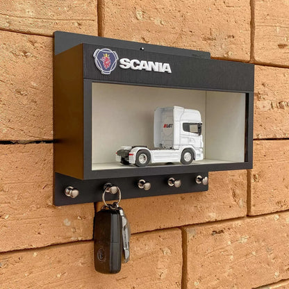 Black rectangular wall-mounted key hook rack with Scania logo and white scale model truck displayed inside transparent front