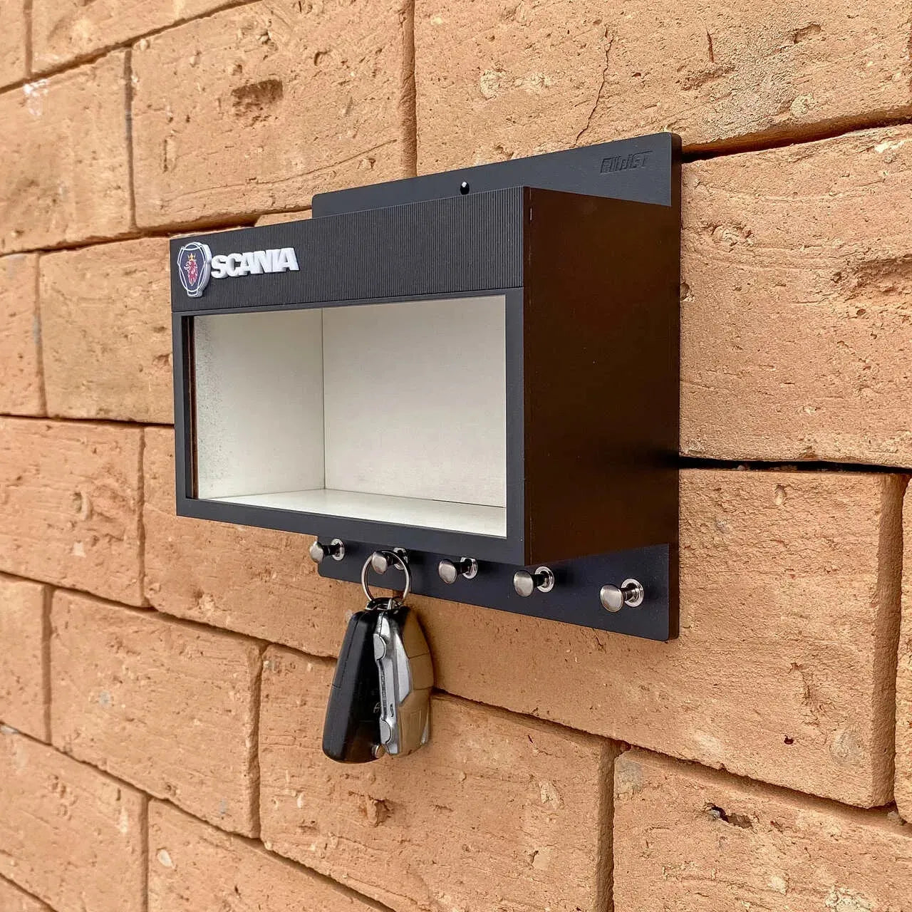 Black metal wall-mounted key hook rack with six silver hooks and a rectangular display case featuring the Scania logo.
