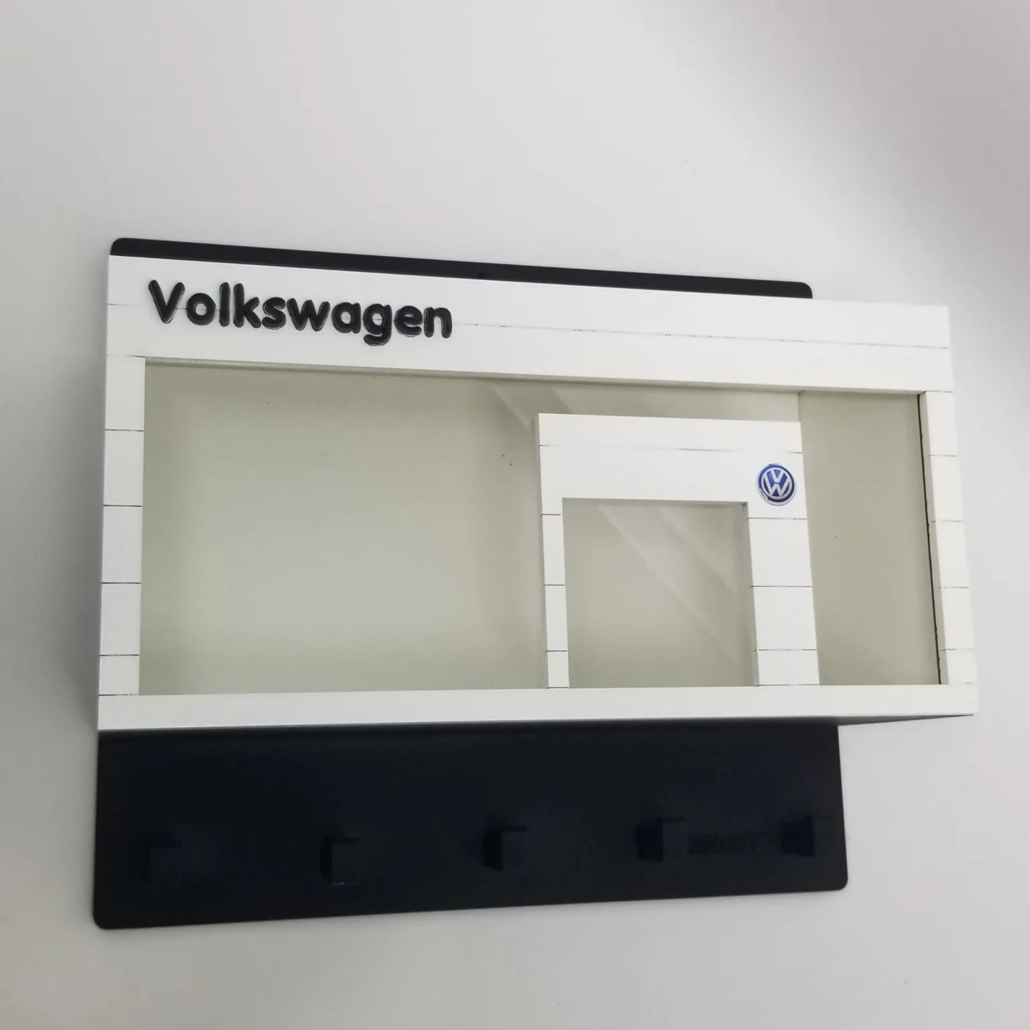 Volkswagen-themed white wall key hook rack with black base and clear display case resembling a car showroom facade.