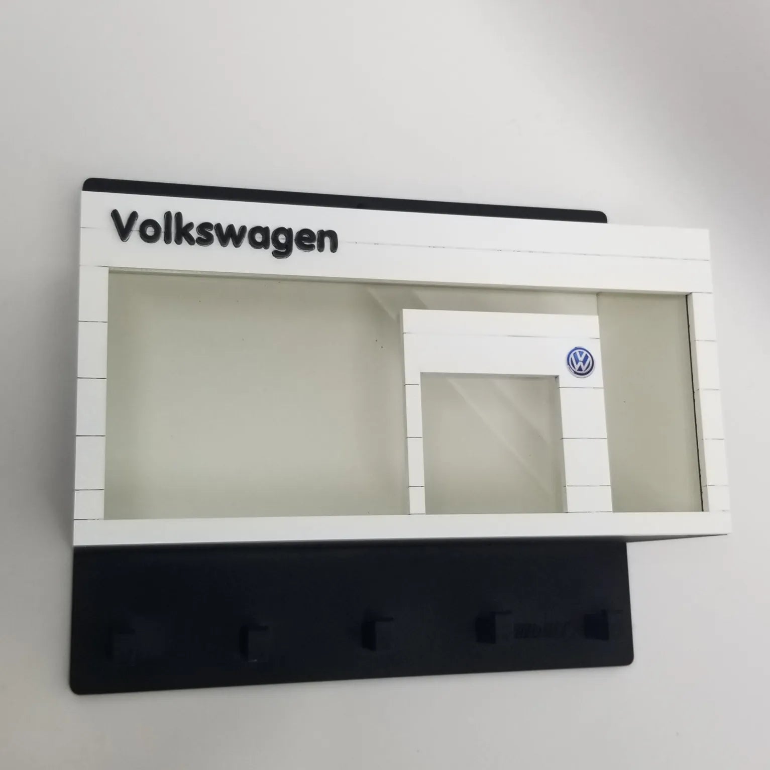 Volkswagen-themed white wall key hook rack with black base and clear display case resembling a car showroom facade.