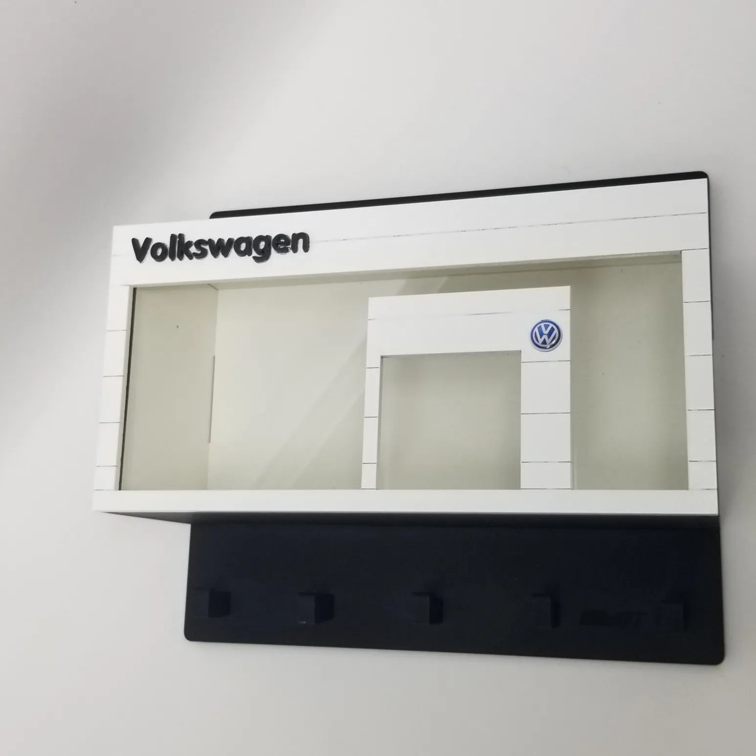 White Volkswagen-themed wall key hook rack with four black hooks and a scale model car display case design.
