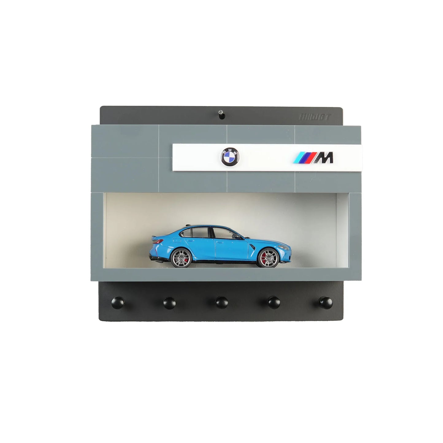Wall-mounted key hook rack designed as a gray BMW M garage with a blue scale model car and four black hooks.