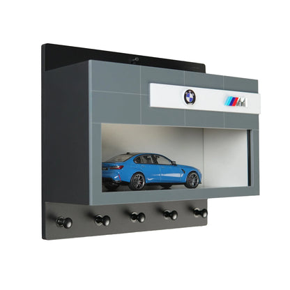 Gray and black wall-mounted BMW display case with a blue scale model car and five black key hooks underneath.
