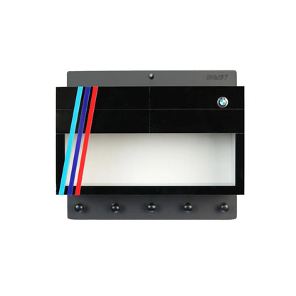 Black wall-mounted key hook rack with four silver hooks, decorated with BMW logo and red, blue, and light blue stripes,.