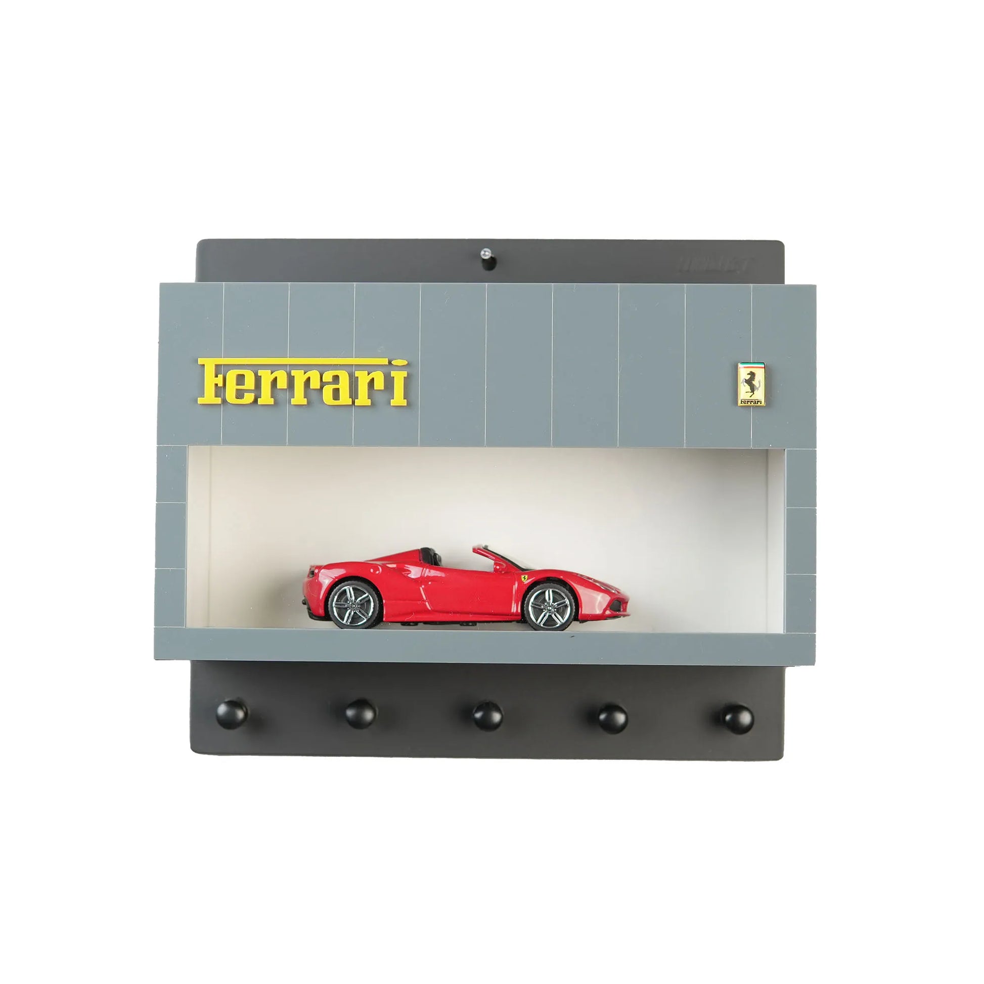 Gray wall-mounted key hook rack with Ferrari logo, model car display case, five black hooks, and red Ferrari sports car.