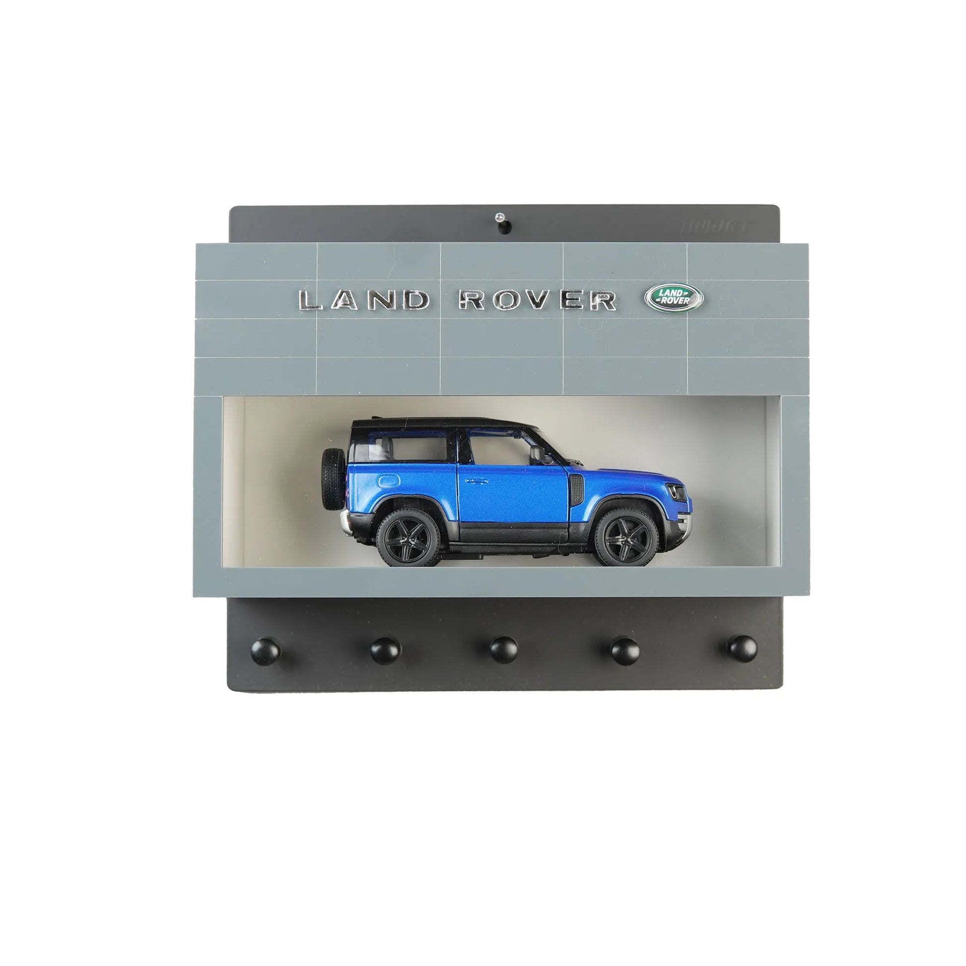 Gray Land Rover wall key hook rack with blue scale model SUV inside display case and five black hooks beneath.