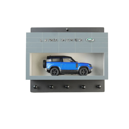 Gray Land Rover wall key hook rack with blue scale model SUV inside display case and five black hooks beneath.