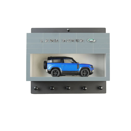 Gray Land Rover wall key hook rack with blue scale model SUV inside display case and five black hooks beneath.