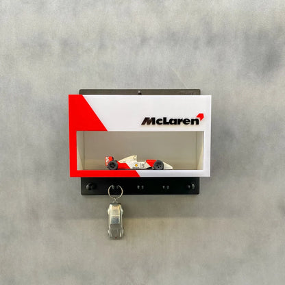 Black wall-mounted key rack with hooks, featuring a McLaren-branded display case and a red and white vintage F1 scale model.