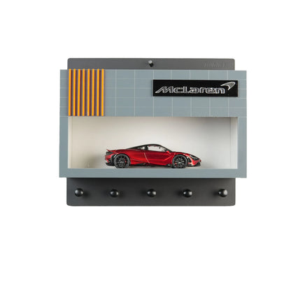Gray and black wall key hook rack with McLaren logo and red scale model car display case.