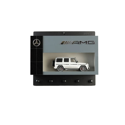 Black and gray Mercedes AMG wall key hook rack with white scale model G-Class SUV and four hooks.