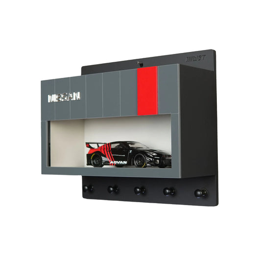 Black and gray Nissan wall key hook rack with a scale model black and red race car in a display case and four hooks below.