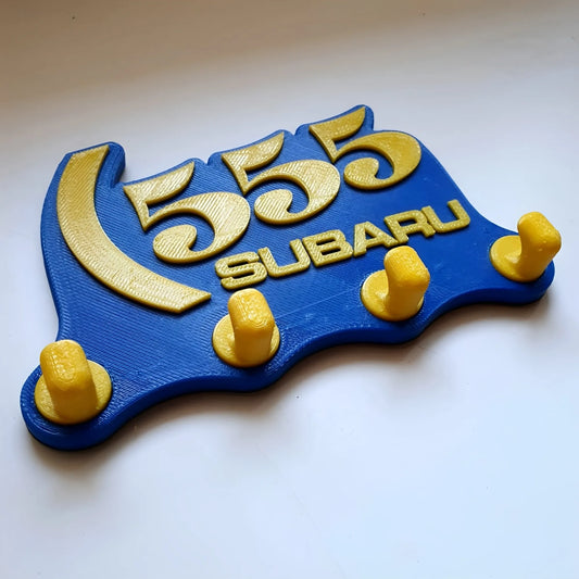 Blue and yellow Subaru 555 wall key hook rack with four yellow hooks and raised logo design.
